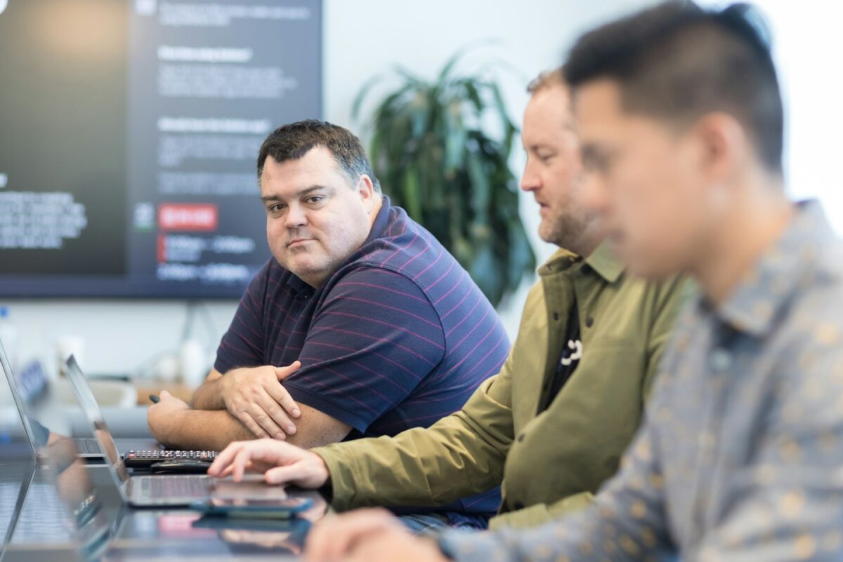 three men sitting at a table with laptops