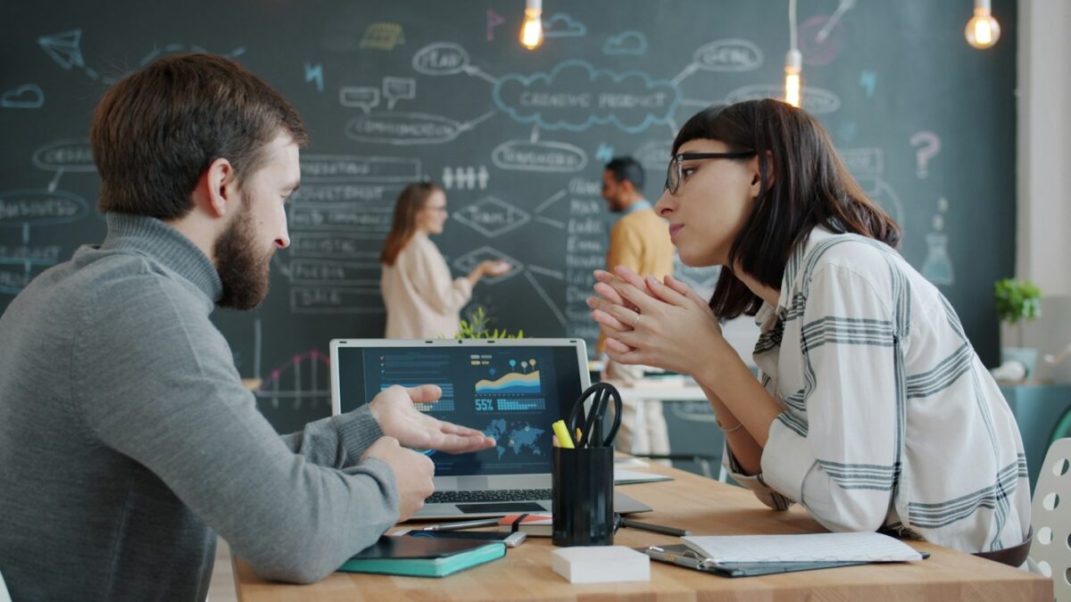Two colleagues discussing charts on a laptop screen
