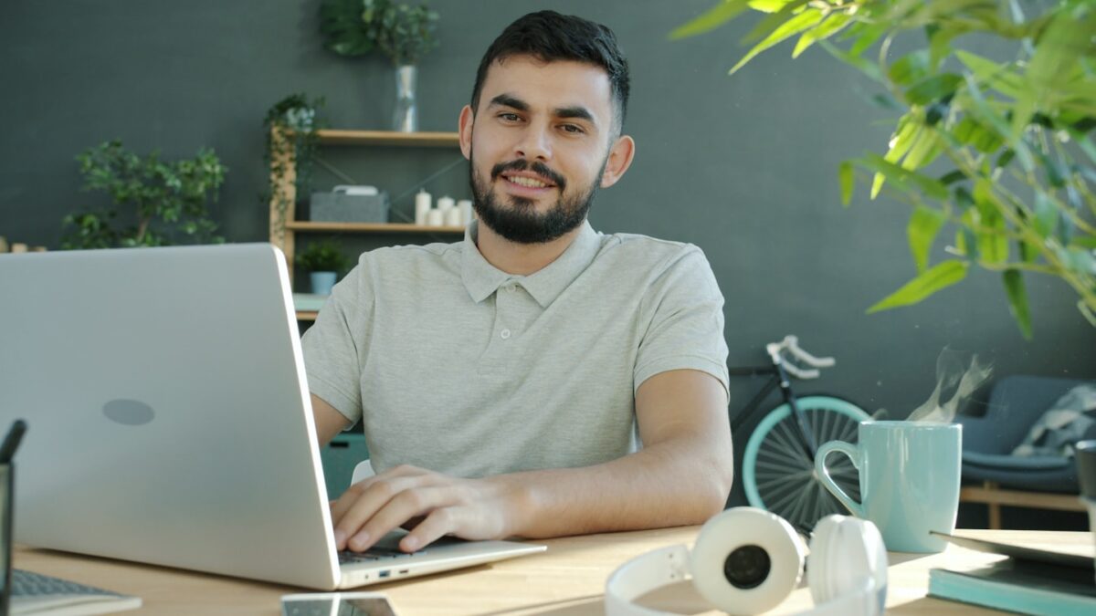 A man smiles while working on a laptop