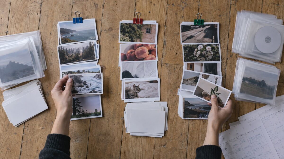 Overhead view of a creator’s hands sorting printed content proofs into three color-clipped groups on a worn wooden floor