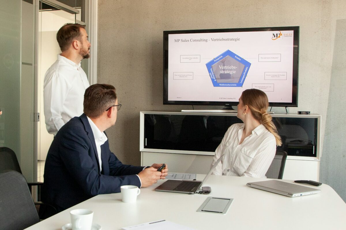Three people in a meeting room looking at a presentation