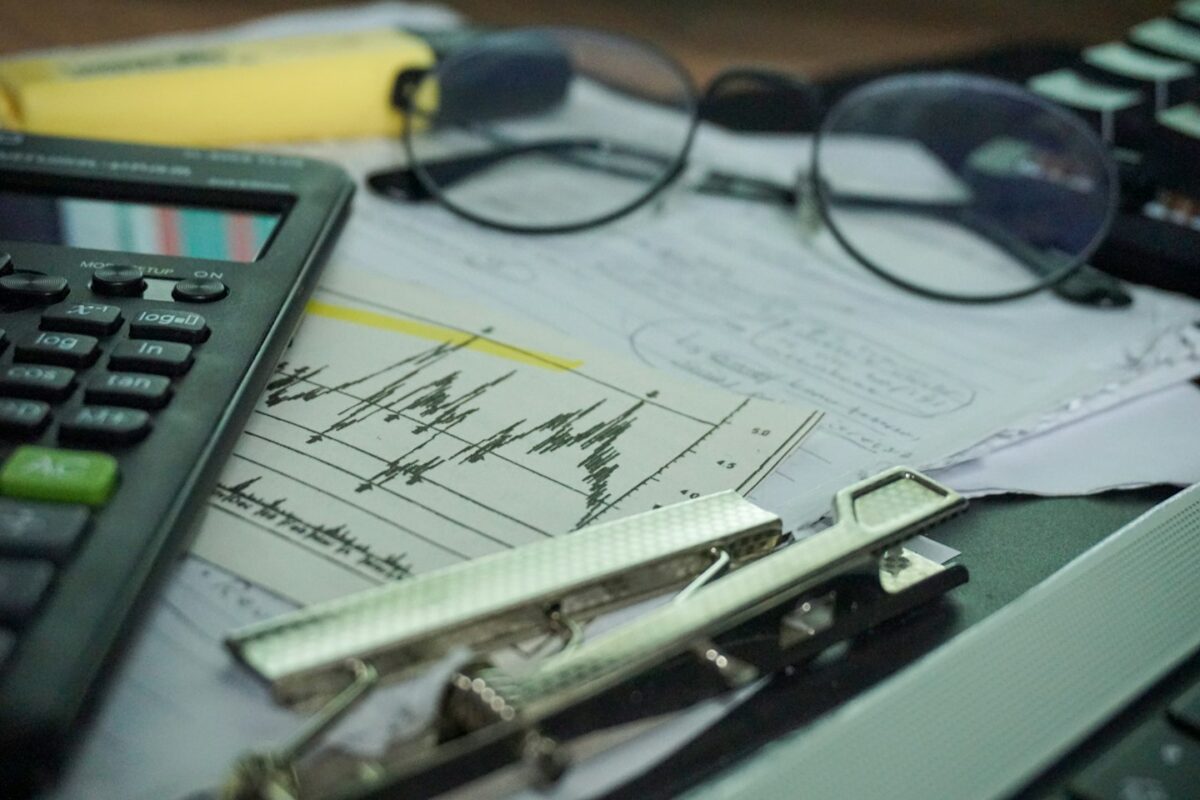 A desk with a calculator, papers, eyeglasses, and office supplies